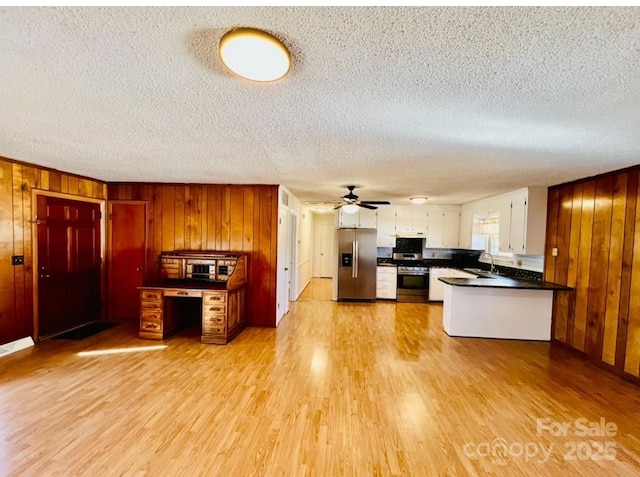 kitchen featuring light hardwood / wood-style flooring, wood walls, a textured ceiling, white cabinets, and appliances with stainless steel finishes