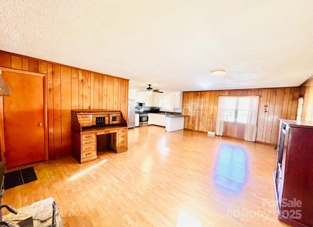 kitchen with kitchen peninsula, wood walls, light wood-type flooring, and appliances with stainless steel finishes