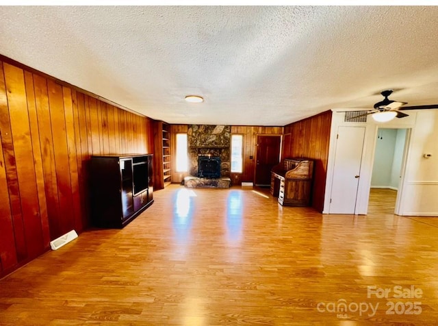 unfurnished living room with ceiling fan, built in shelves, a fireplace, a textured ceiling, and light hardwood / wood-style floors