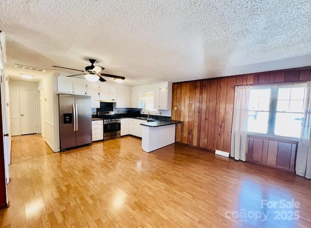 kitchen with white cabinets, wooden walls, stainless steel appliances, and a wealth of natural light