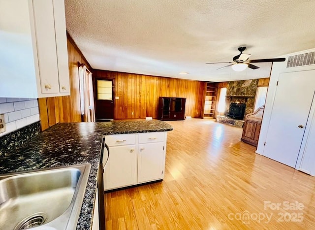 kitchen featuring light wood-type flooring, a textured ceiling, ceiling fan, a fireplace, and white cabinetry