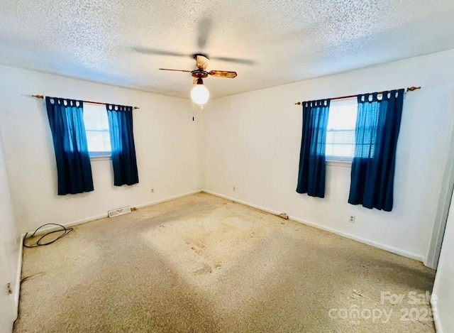 carpeted spare room with ceiling fan, a healthy amount of sunlight, and a textured ceiling