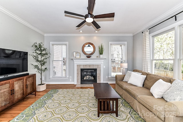 living room with a tile fireplace, ornamental molding, ceiling fan, and light hardwood / wood-style flooring