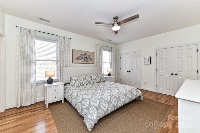 bedroom with ceiling fan, two closets, and light wood-type flooring