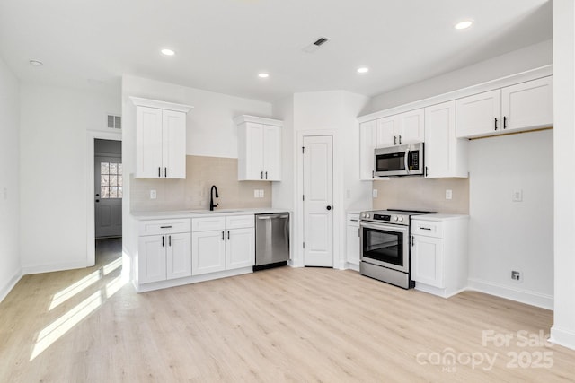 kitchen with white cabinets, sink, decorative backsplash, light hardwood / wood-style floors, and stainless steel appliances