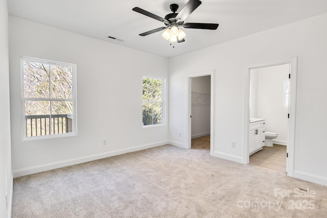 unfurnished bedroom featuring ceiling fan, ensuite bathroom, a walk in closet, light carpet, and a closet