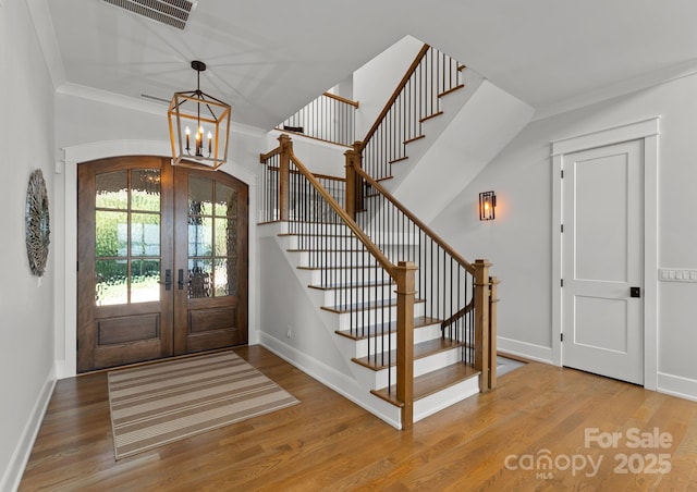 foyer with hardwood / wood-style flooring, an inviting chandelier, ornamental molding, and french doors