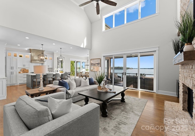 living room with a high ceiling, a water view, ceiling fan, a fireplace, and light hardwood / wood-style floors