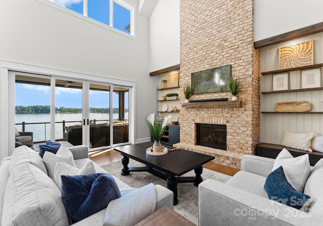 living room with a high ceiling, french doors, a water view, light wood-type flooring, and a fireplace