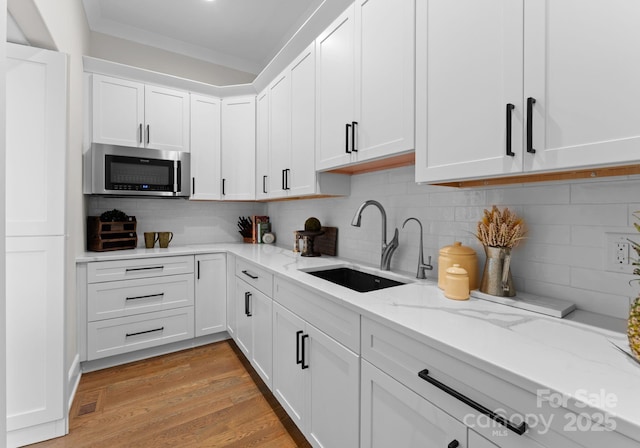 kitchen featuring backsplash, sink, light hardwood / wood-style floors, light stone counters, and white cabinetry