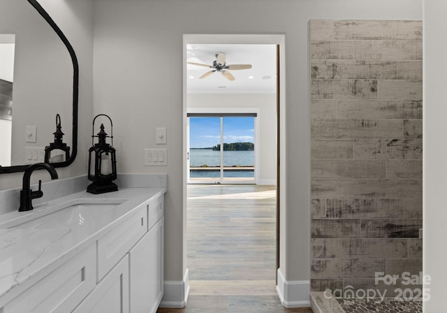 bathroom featuring ceiling fan, a shower, wood-type flooring, a water view, and vanity