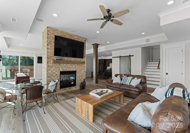 living room with light wood-type flooring, a stone fireplace, ceiling fan, and a barn door