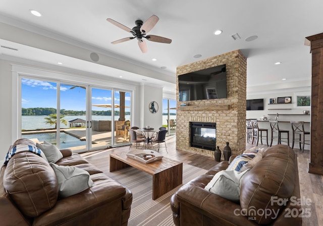 living room featuring ceiling fan, a water view, ornamental molding, and a brick fireplace