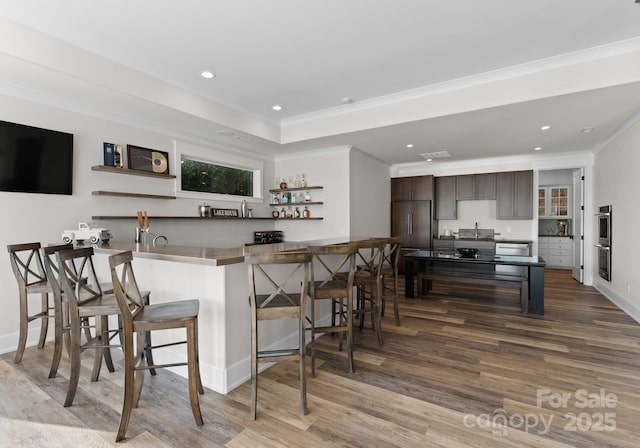 bar featuring sink, light hardwood / wood-style flooring, ornamental molding, double oven, and dark brown cabinetry