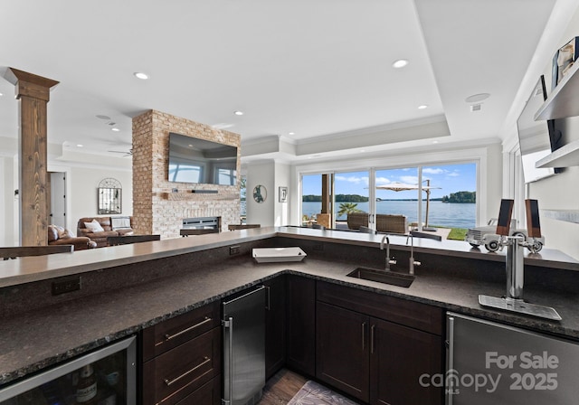 kitchen with ornate columns, sink, wine cooler, a stone fireplace, and ornamental molding