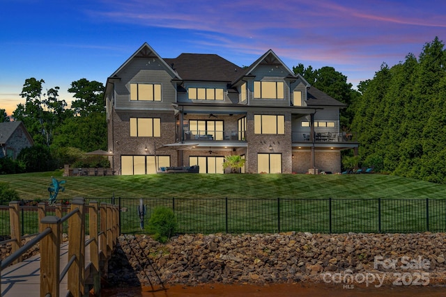 back house at dusk featuring a lawn, ceiling fan, and a balcony