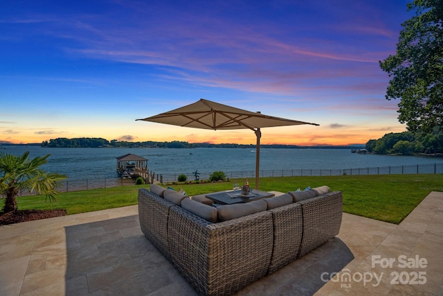 patio terrace at dusk featuring a water view and a lawn