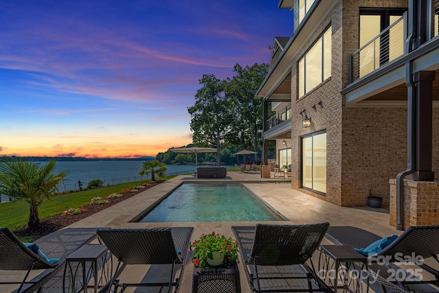 pool at dusk with a water view and a patio