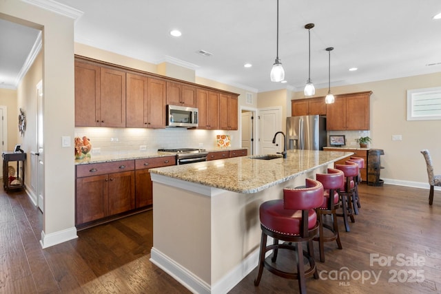 kitchen with a center island with sink, appliances with stainless steel finishes, light stone counters, a breakfast bar, and sink