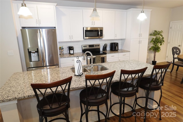 kitchen featuring a kitchen breakfast bar, a center island with sink, stainless steel appliances, white cabinets, and backsplash