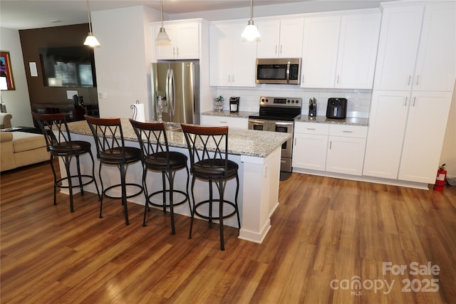 kitchen featuring a center island with sink, white cabinets, hanging light fixtures, and appliances with stainless steel finishes