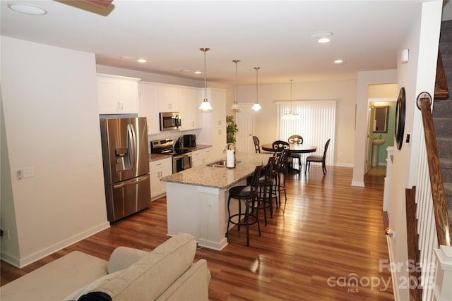kitchen featuring appliances with stainless steel finishes, an island with sink, pendant lighting, sink, and white cabinetry