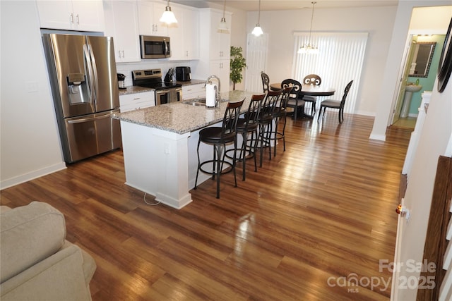 kitchen featuring a center island with sink, appliances with stainless steel finishes, a kitchen bar, sink, and decorative light fixtures