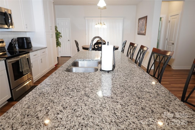 kitchen featuring sink, hanging light fixtures, light stone counters, white cabinets, and appliances with stainless steel finishes