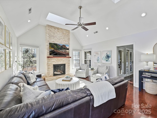 living room with ceiling fan, dark wood-type flooring, a stone fireplace, and a healthy amount of sunlight