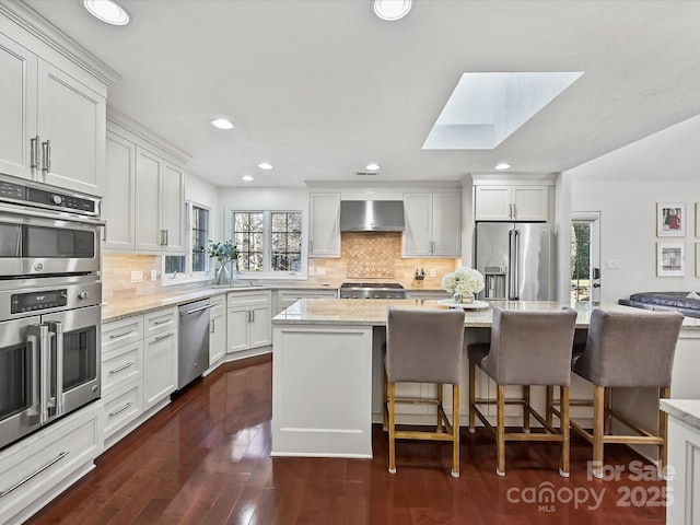 kitchen with white cabinetry, a skylight, wall chimney exhaust hood, and stainless steel appliances