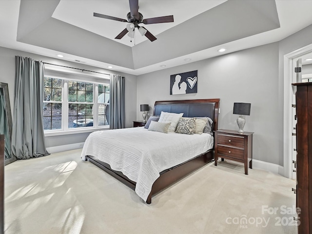 bedroom with light carpet, ceiling fan, and a raised ceiling