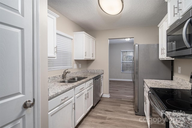 kitchen featuring appliances with stainless steel finishes, light wood-type flooring, light stone countertops, white cabinets, and sink