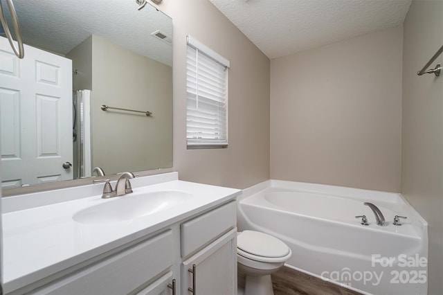 bathroom featuring a textured ceiling, a tub to relax in, vanity, and toilet