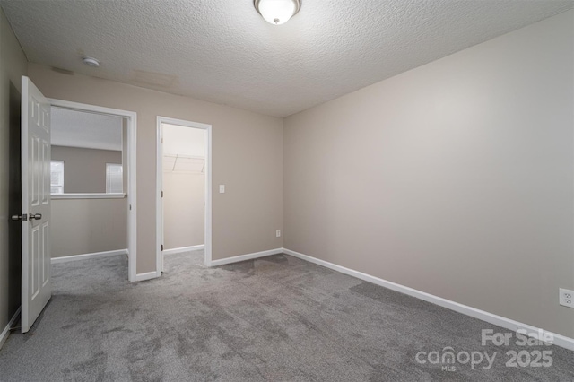 unfurnished bedroom featuring a spacious closet, light colored carpet, a textured ceiling, and a closet