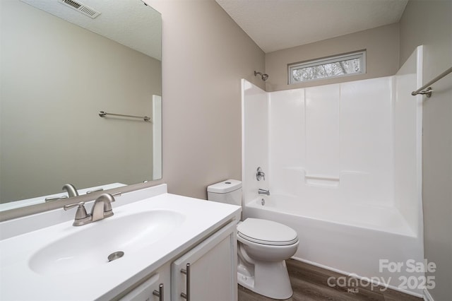 full bathroom featuring a textured ceiling, bathing tub / shower combination, wood-type flooring, vanity, and toilet