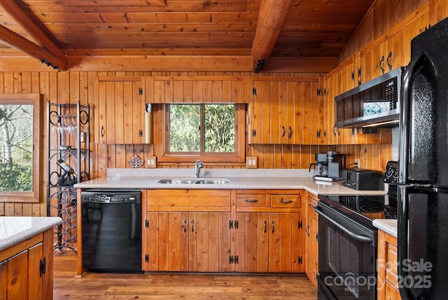 kitchen featuring black appliances, light wood-type flooring, sink, and wooden walls