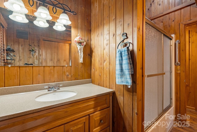 bathroom with wood walls, vanity, and combined bath / shower with glass door