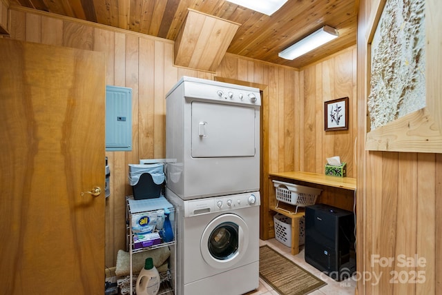 clothes washing area with wooden walls, wooden ceiling, stacked washer and clothes dryer, electric panel, and light tile patterned flooring