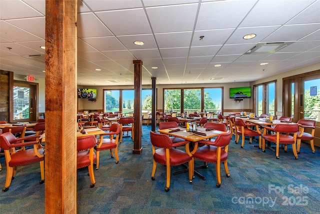 dining area featuring a wealth of natural light, a drop ceiling, and dark colored carpet