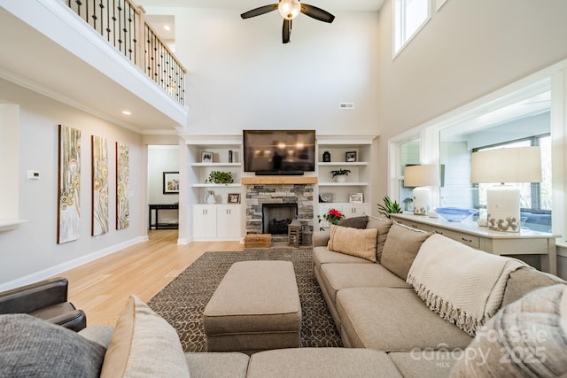 living room with light wood-type flooring, a towering ceiling, a stone fireplace, and built in shelves