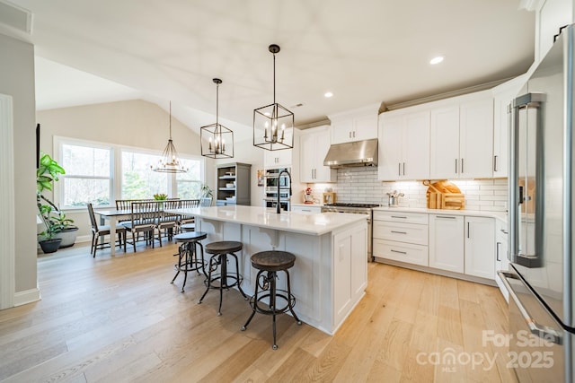 kitchen featuring vaulted ceiling, pendant lighting, a center island with sink, high end appliances, and white cabinets