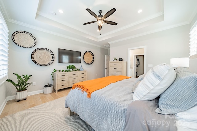 bedroom with ceiling fan, a tray ceiling, and light hardwood / wood-style floors