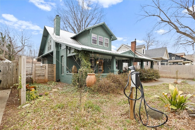 view of front of home featuring metal roof, covered porch, a chimney, and fence