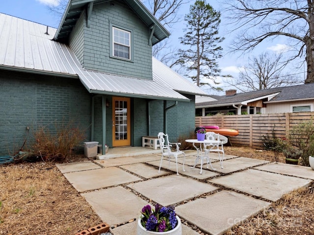 rear view of property with metal roof, a patio, brick siding, and fence