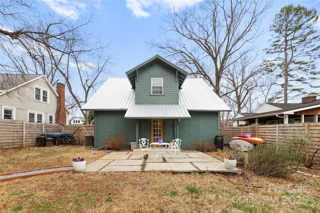 back of house featuring a patio, a fenced backyard, brick siding, and metal roof