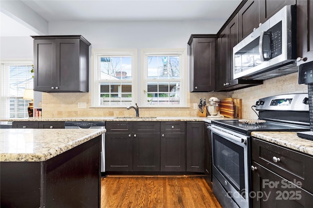 kitchen with a sink, light stone countertops, appliances with stainless steel finishes, and dark wood-style flooring