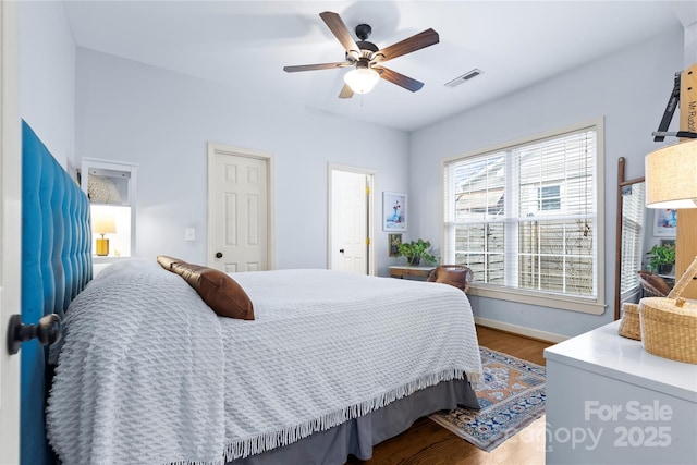 bedroom with ceiling fan, visible vents, baseboards, and wood finished floors