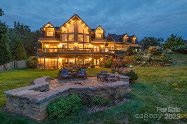 back house at dusk featuring a lawn, a patio area, and a deck