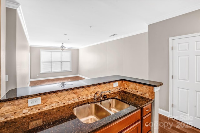 kitchen featuring sink, ornamental molding, ceiling fan, dark stone counters, and dark hardwood / wood-style flooring