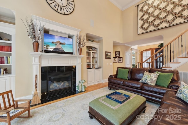 living room with hardwood / wood-style flooring, built in features, crown molding, and a tiled fireplace